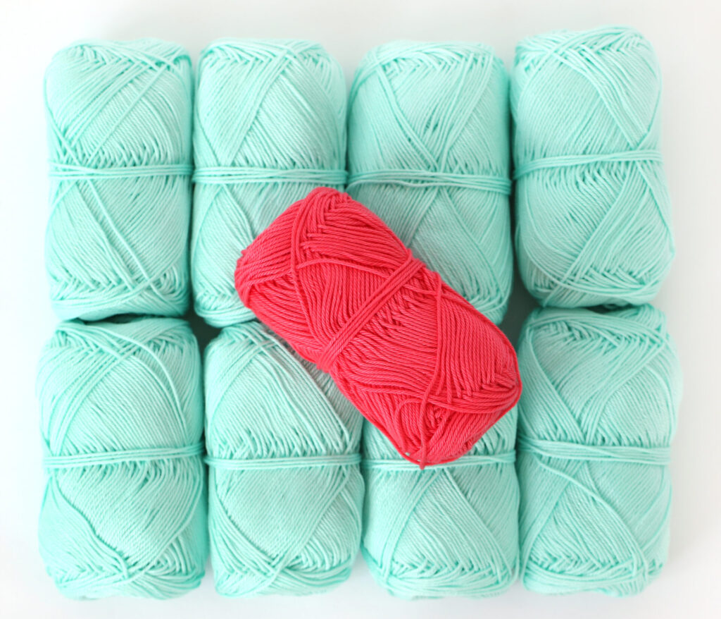 Schachenmayr yarn type Catania, 8 mentol colored balls are laying down in 2x4 square and y bright red colored ball lays on the top of the others