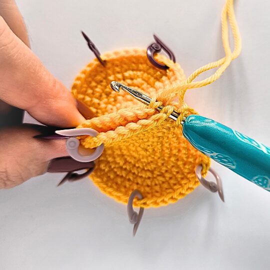 Crochet a star, hook is in bright blue, star is in yellov, one hand is holding a star body - joining two parts together