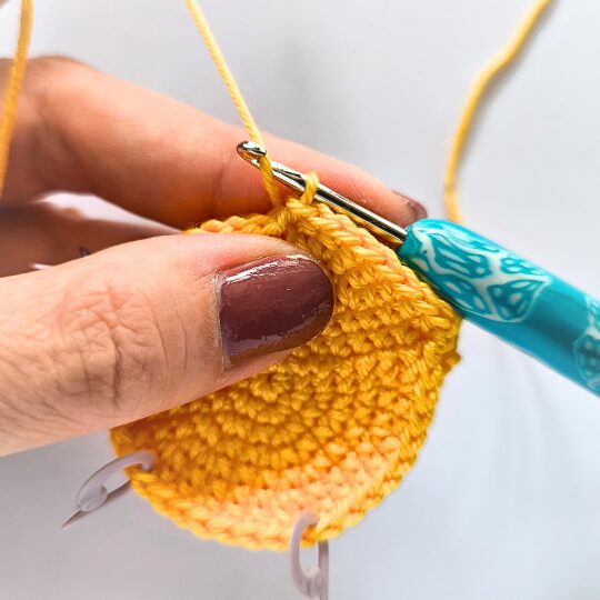 Crochet a star, hook is in bright blue, star is in yellov, one hand is holding a star body