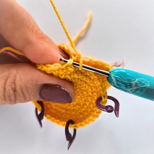 Crochet a star, hook is in bright blue, star is in yellov, one hand is holding a star body