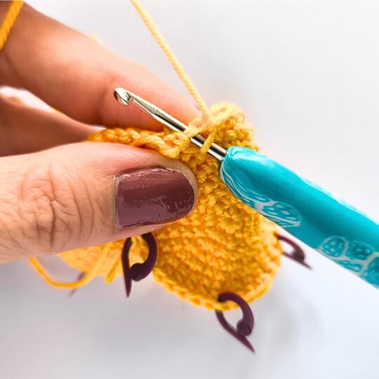Crochet a star, hook is in bright blue, star is in yellov, one hand is holding a star body