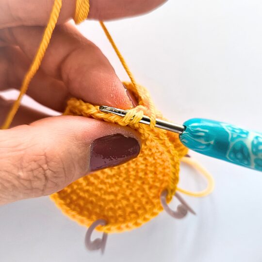 Crochet a star, hook is in bright blue, star is in yellov, one hand is holding a star body