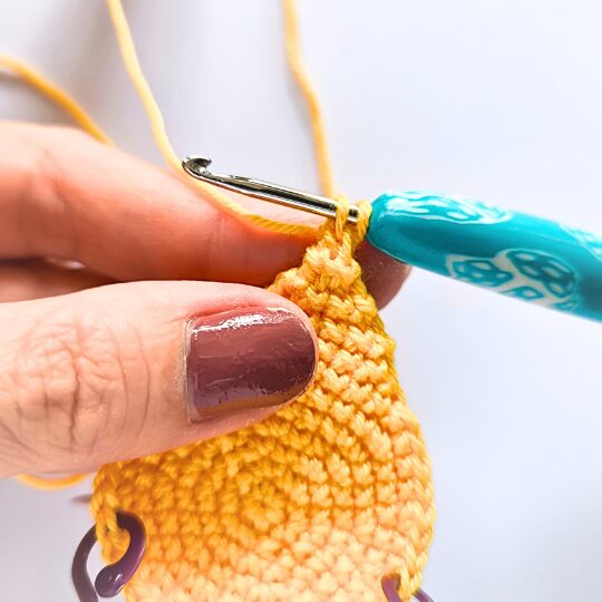Crochet a star, hook is in bright blue, star is in yellov, one hand is holding a star body - finishing spike