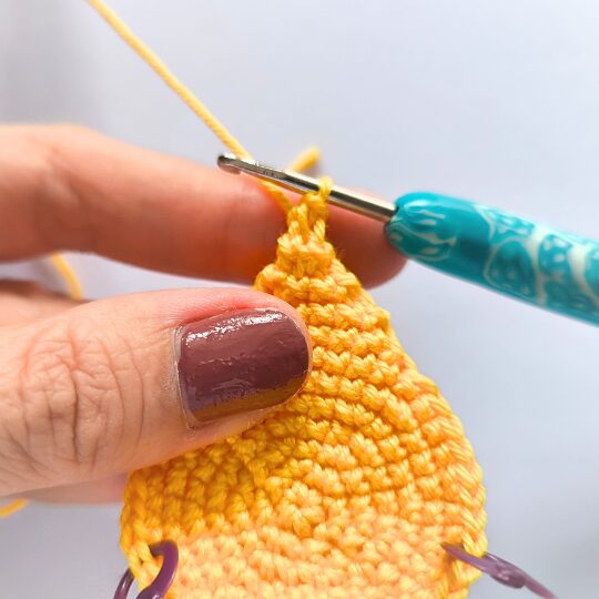 Crochet a star, hook is in bright blue, star is in yellov, one hand is holding a star body - finishing spike