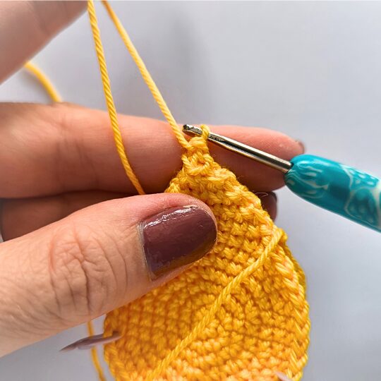 Crochet a star, hook is in bright blue, star is in yellov, one hand is holding a star body - finishing spike