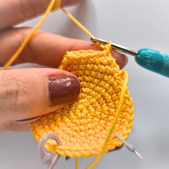 Crochet a star, hook is in bright blue, star is in yellov, one hand is holding a star body