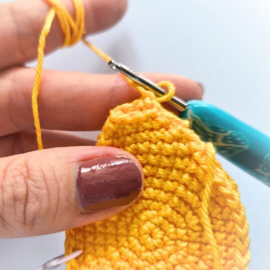 Crochet a star, hook is in bright blue, star is in yellov, one hand is holding a star body