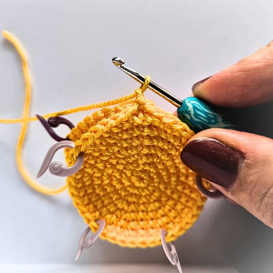 Crochet a star, hook is in bright blue, star is in yellov, one hand is holding a star body