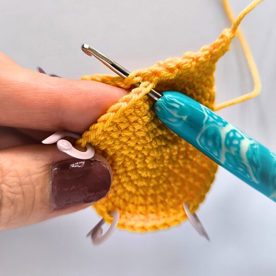 Crochet a star, hook is in bright blue, star is in yellov, one hand is holding a star body