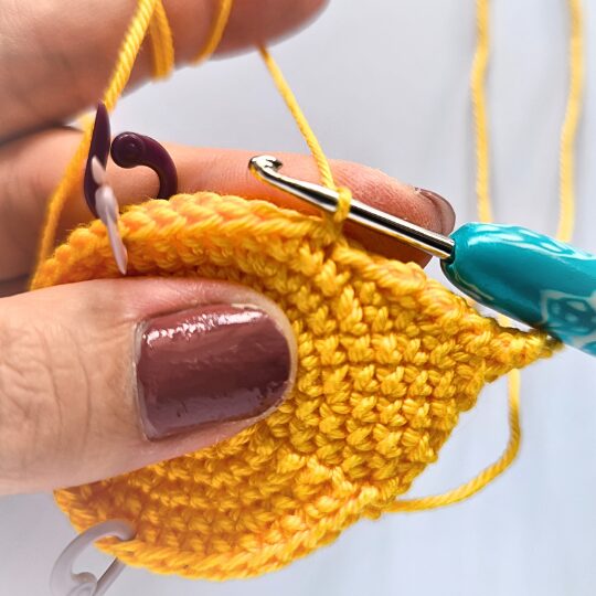 Crochet a star, hook is in bright blue, star is in yellov, one hand is holding a star body