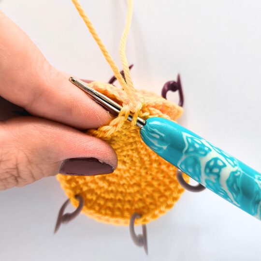 Crochet a star, hook is in bright blue, star is in yellov, one hand is holding a star body - joining two parts together