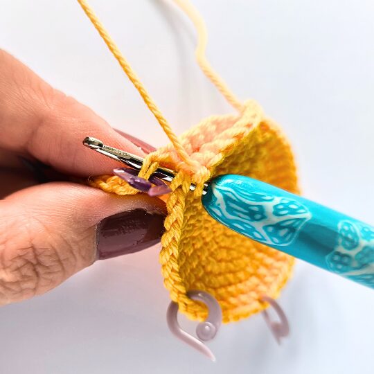 Crochet a star, hook is in bright blue, star is in yellov, one hand is holding a star body - joining two parts together