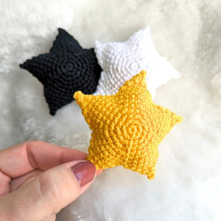 Hand holding yellow crochet star. Behind it are two stars in white and black colors