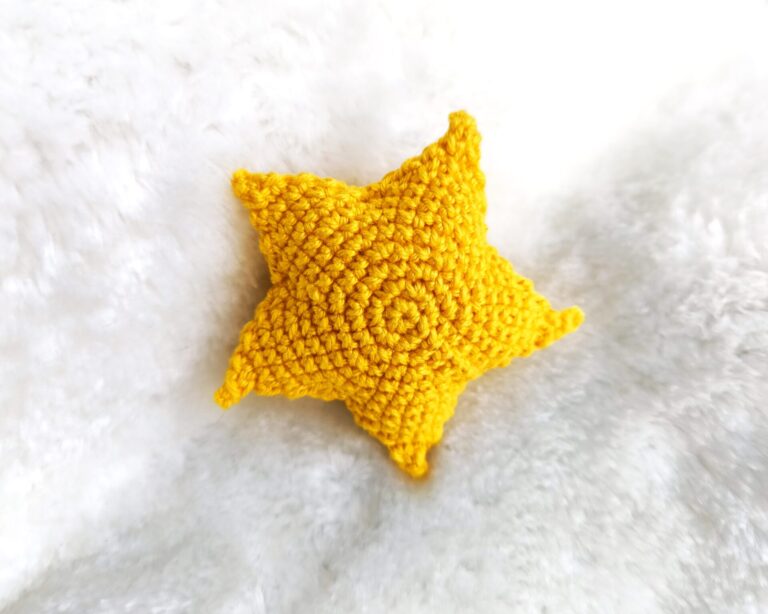 Crochet stuffed star in yellow with five spikes laying on the fauch white fur